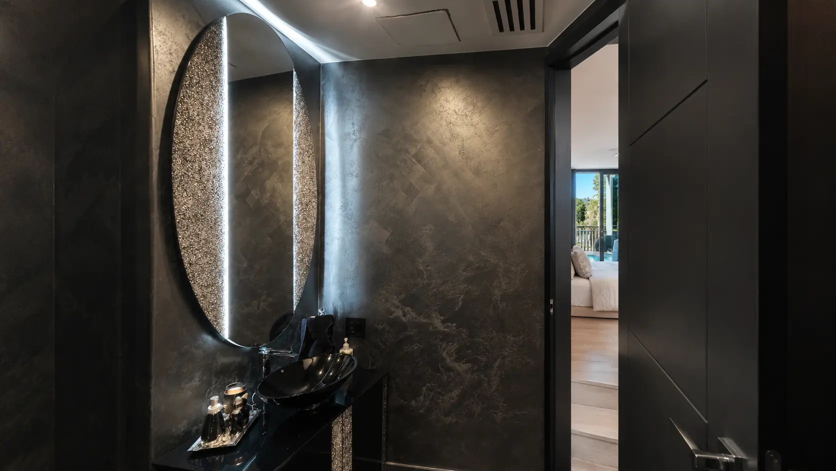 Powder room with dark metallic plaster walls and a backlit oval mirror